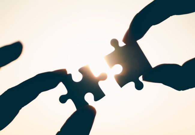 Silhouette of closeup woman and man hand connecting a piece of jigsaw puzzle over sunlight effect. symbol of association and connection concept. business strategy.